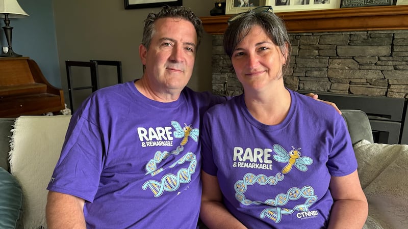 A man and a woman pose for a photo while wearing purple shirts.