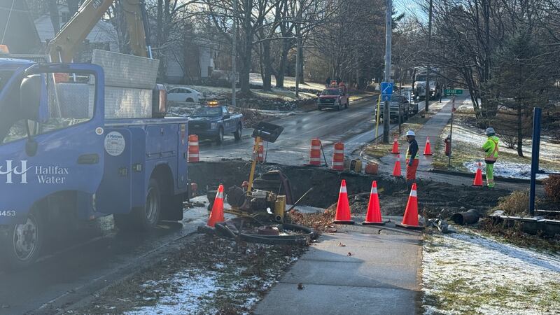 A blue truck is pictured next to pylons which surround a sinkhole in the road.