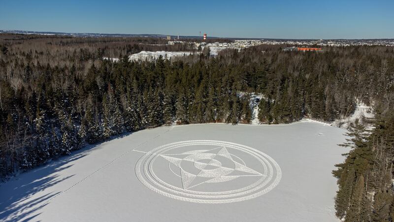 A frozen lake covered in snow is pictured surrounded by trees.