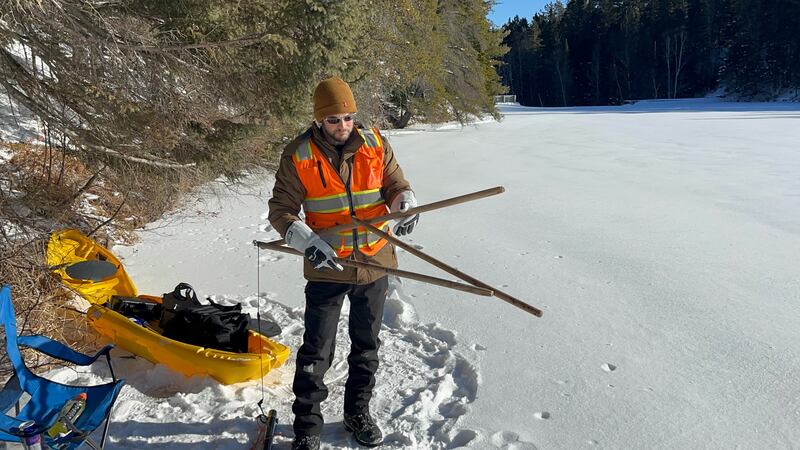 A man wearing winter gear and an orange vest holds a pair of snowshoes.