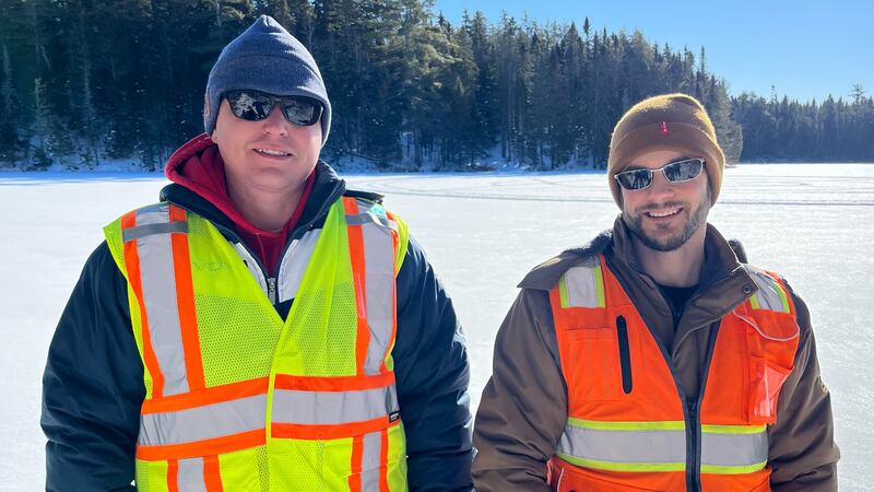 Two men wearing winter coats and hats are also wearing reflective vests.