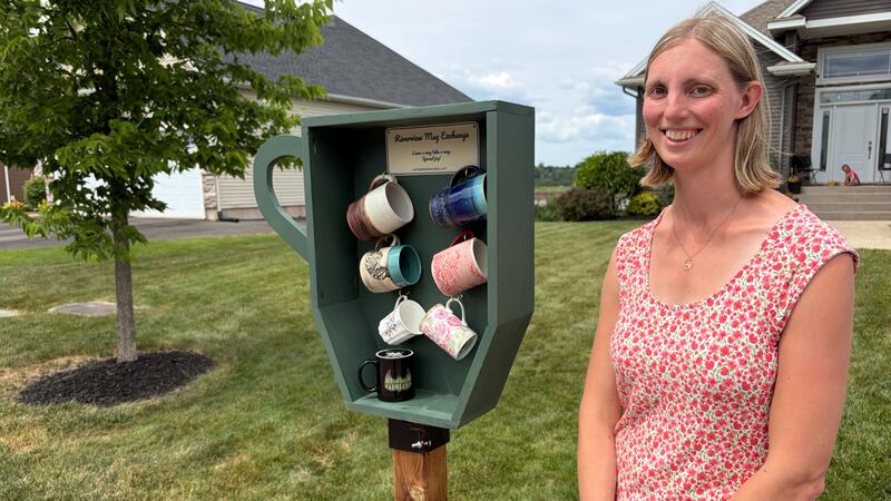 A woman stands next to a coffee mug holder outside.