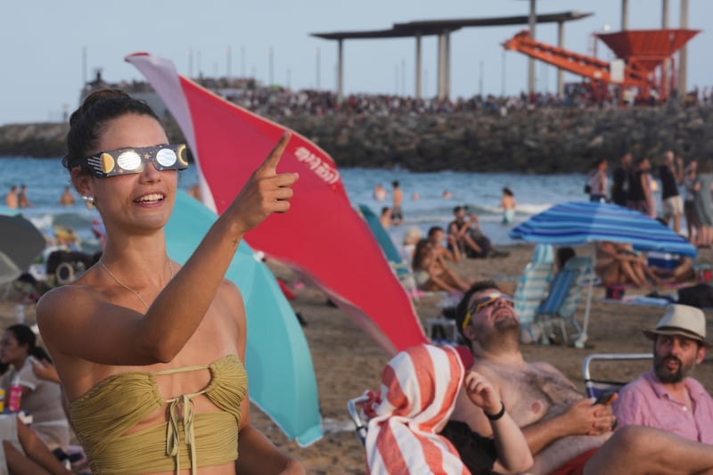 A beachgoer wearing special eclipse glasses points skyward before the partial phase of the solar eclipse at Puerto de Sagunto beach near Valencia, Spain on Aug. 12, 2026. (Alberto Saiz / AP Photo)