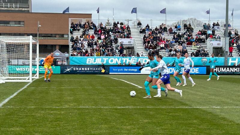 Women's soccer players compete on a field in front of a crowd.
