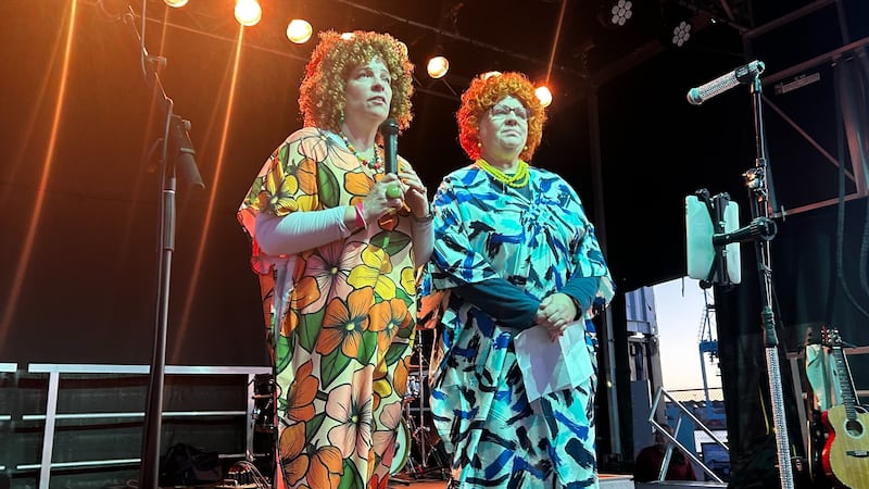 Two women stand on a stage dressed as Mrs. Roper.