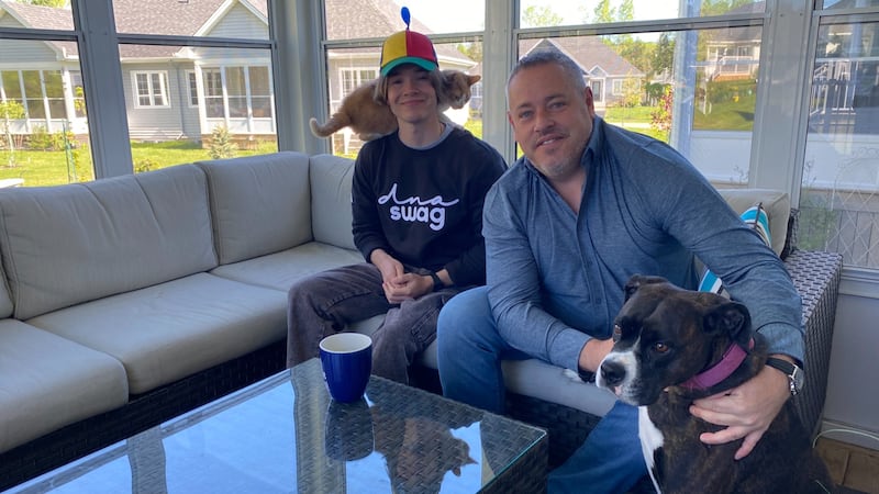 A young man sits next to and older man, along with a cat and dog.