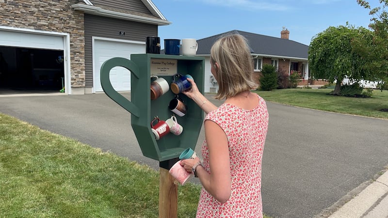 A woman looks at coffee mugs in an outdoor library.