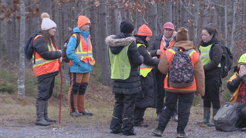 A group of people stand together wearing parkas, toques and high visibility vests.