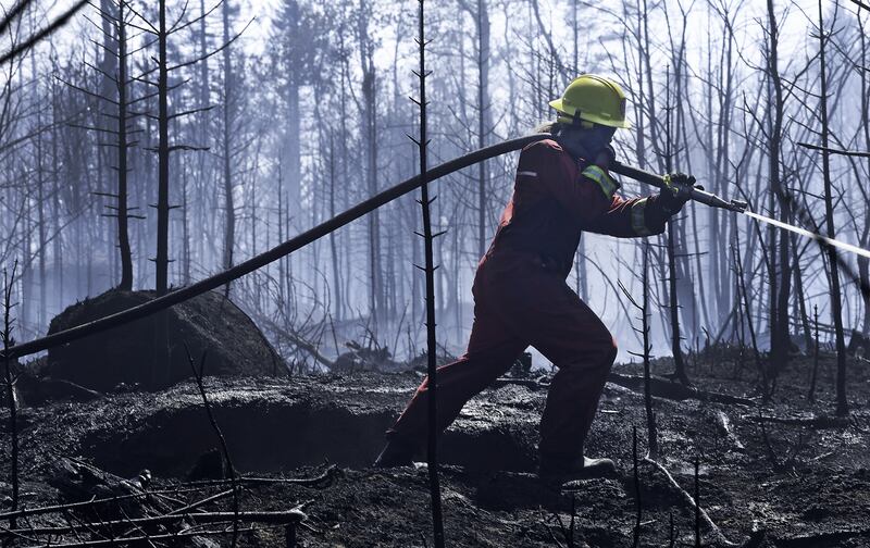 A woman sprays down a burnt out area around a communications tower near the Long Lake wildfire. (Government of Nova Scotia)