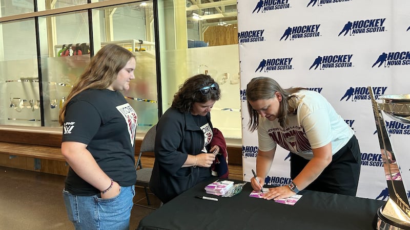 A woman signs autographs for two other women.