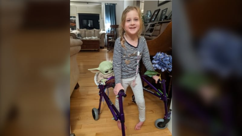 A little girl uses a purple walker.