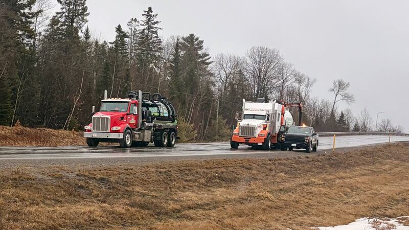 Two large trucks are pictured on a road next to a pickup truck.