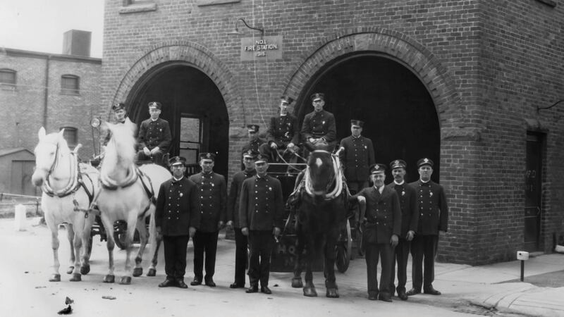 Firefighters are pictured with horses in a black and white photo.
