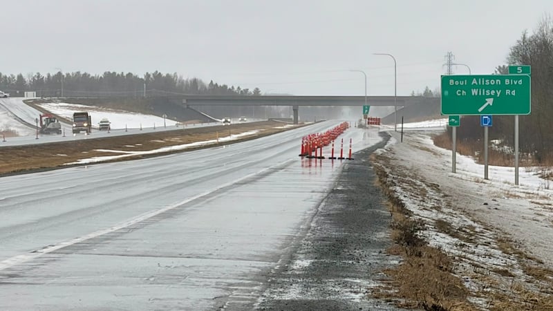 A wet highway is pictured with pylons blocking a lane.