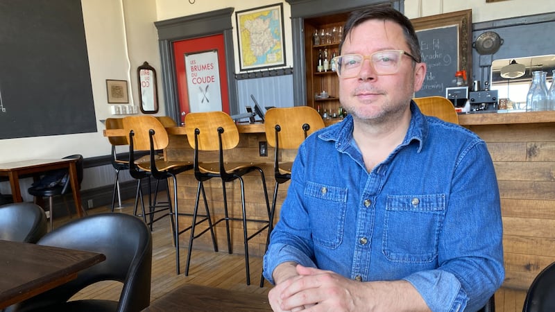 A man in a blue denim shirt is pictured sitting at a table.