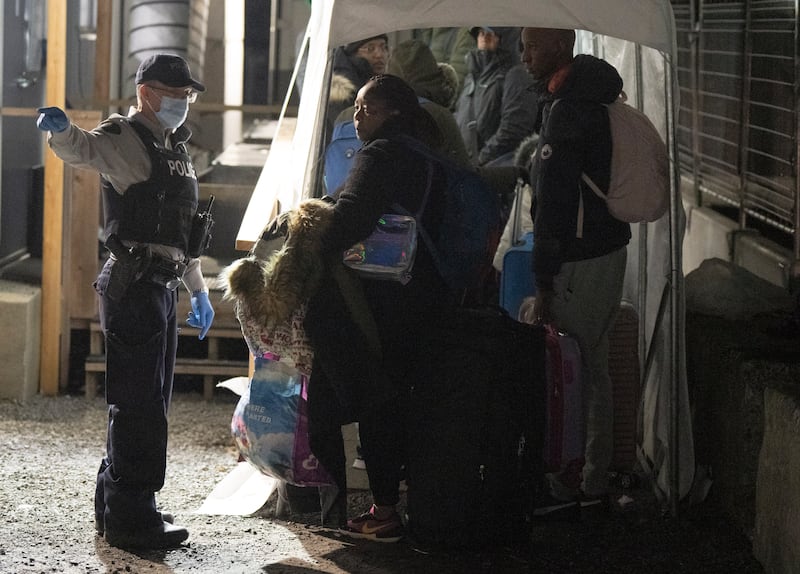 An RCMP officer instructs asylum seekers as they wait for processing after crossing the border at Roxham Road from New York into Canada in Champlain, N.Y., on March 24, 2023. (Ryan Remiorz / The Canadian Press)