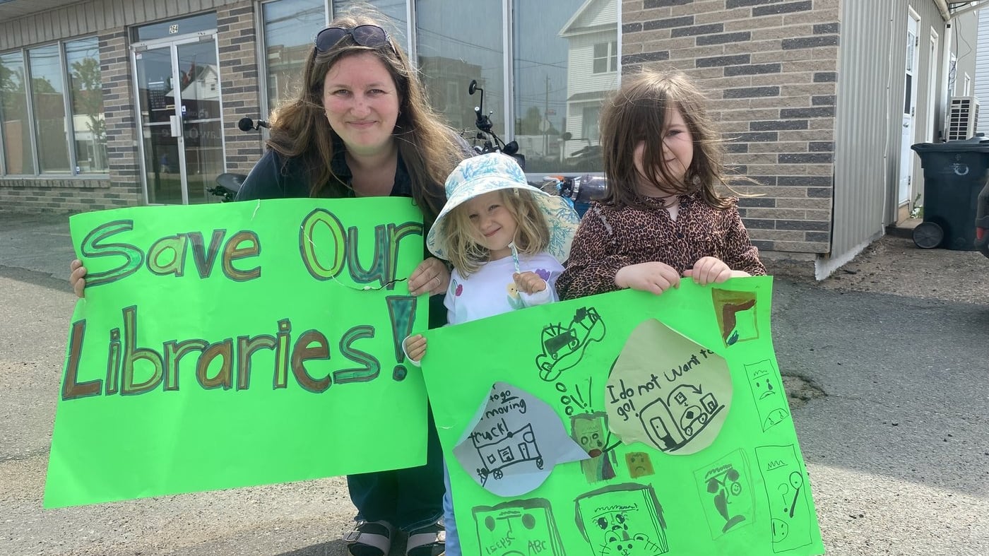 Krista Arsenault and her daughters Evie and Alice Arsenault pose with signs they made for a rally to save five rural libraries in their county that are slated to close next month, in Middleton, N.S., on Friday, June 5, 2026. THE CANADIAN PRESS/Lyndsay Armstrong